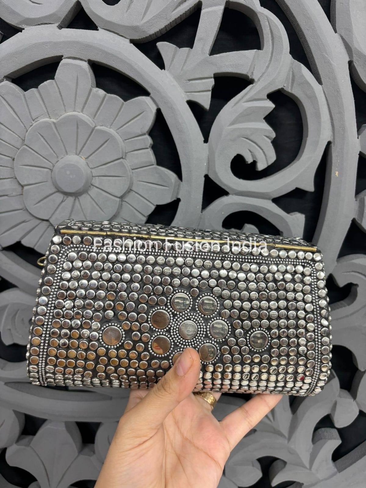 Silver studded clutch held by a hand against a decorative gray background