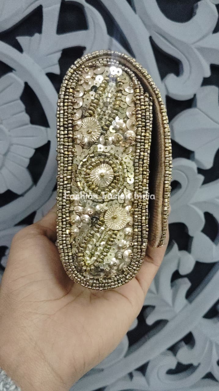 Gold beaded clutch held by a hand against a decorative white and black background