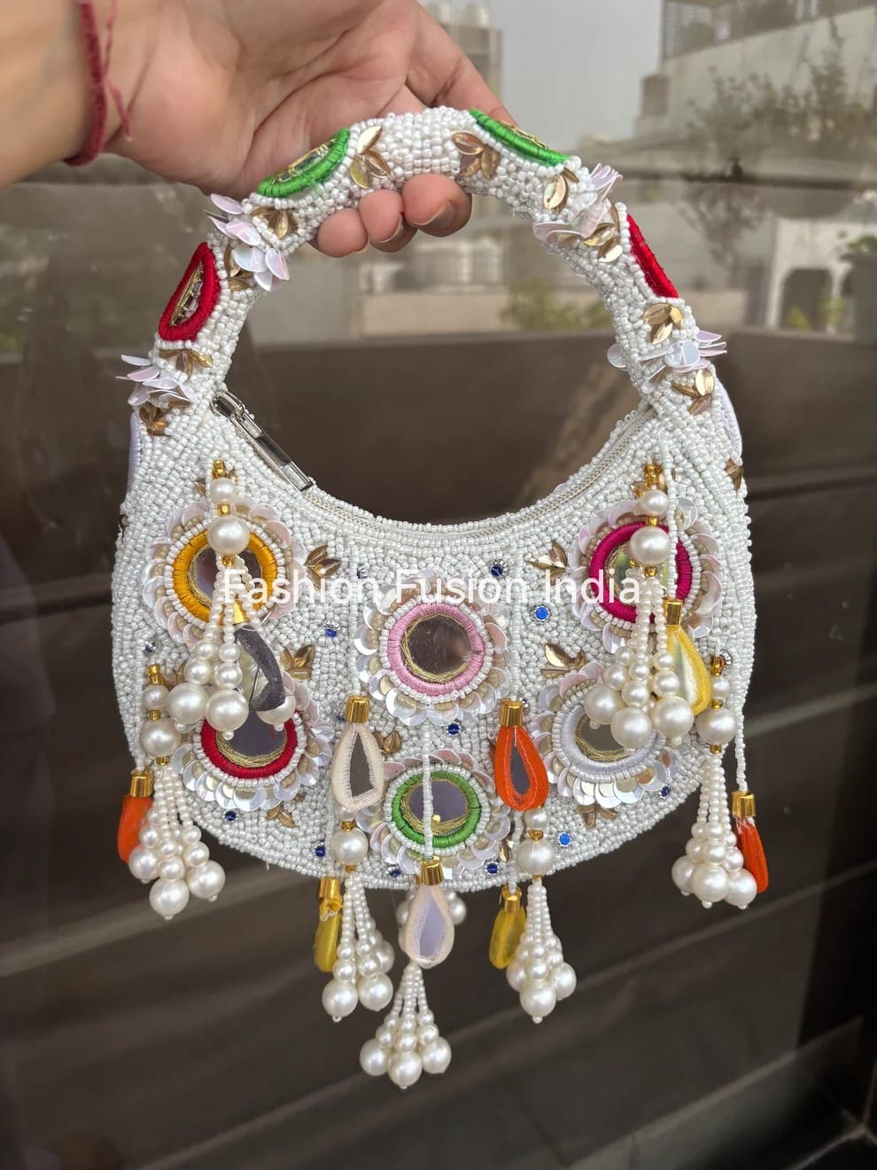 Decorative handbag with intricate designs and beads held by a hand against a blurred background.