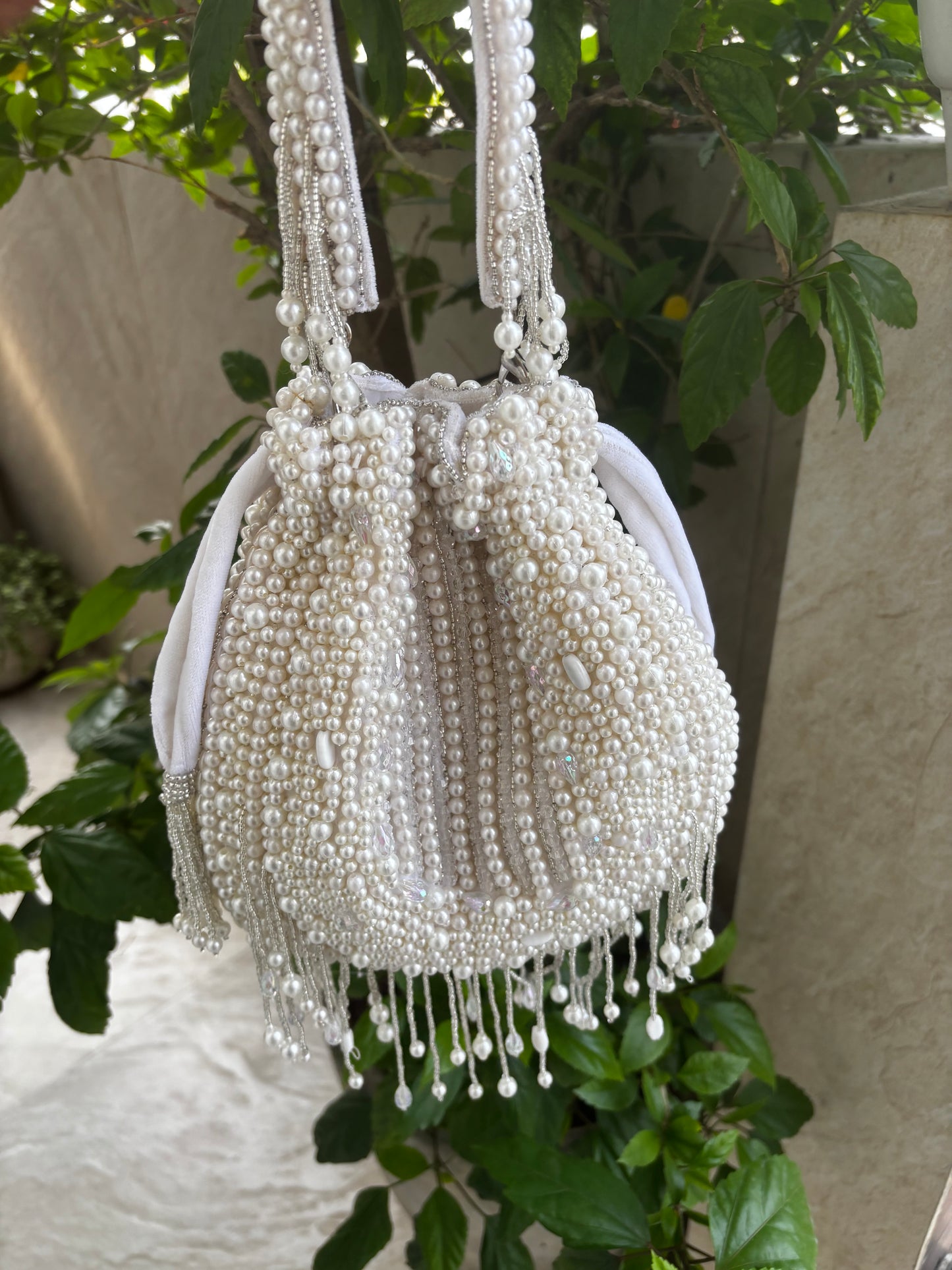 White beaded handbag on a mannequin with green foliage in the background