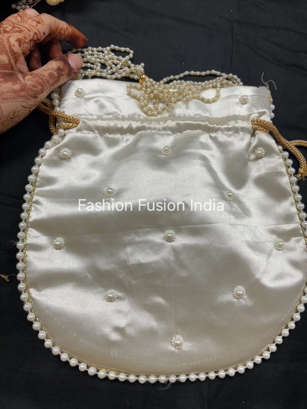 White handbag with pearl embellishments held by a hand with henna designs on a black background, branded 'Fashion Fusion India'.