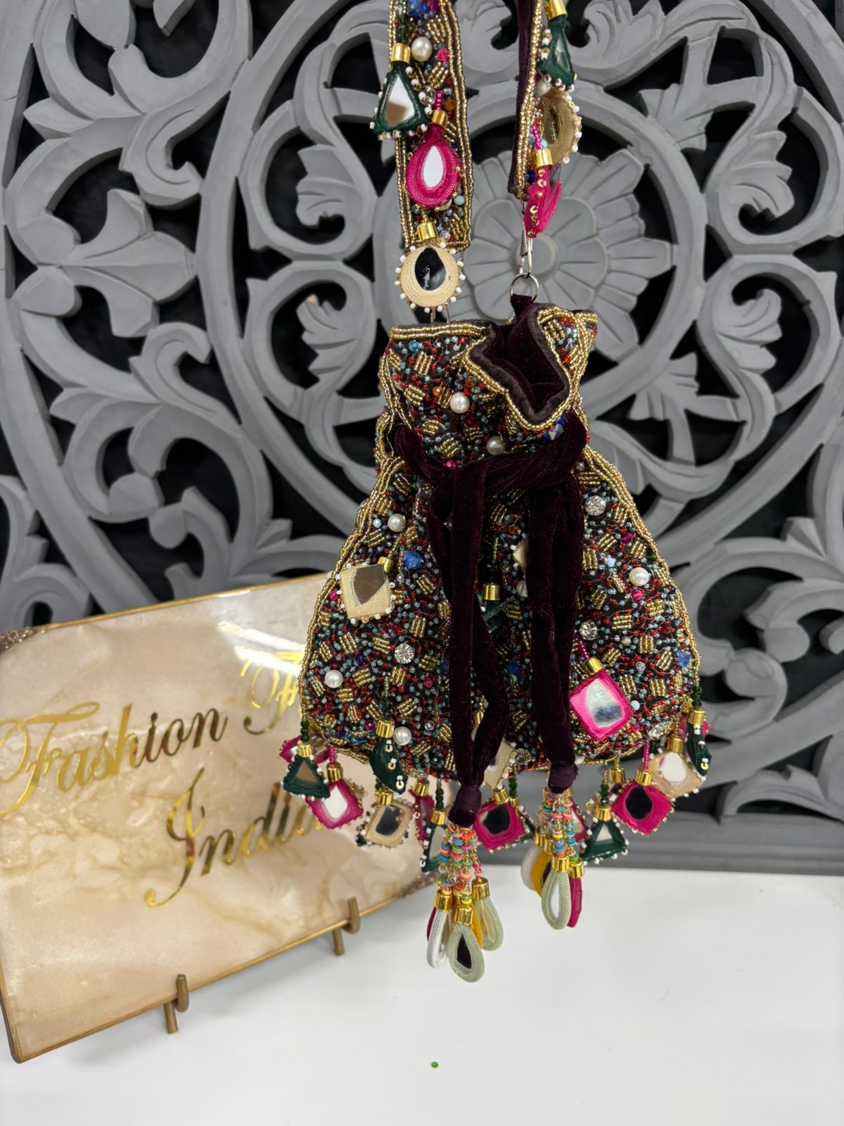 Decorative earring with gemstones on a stand against a decorative wall.