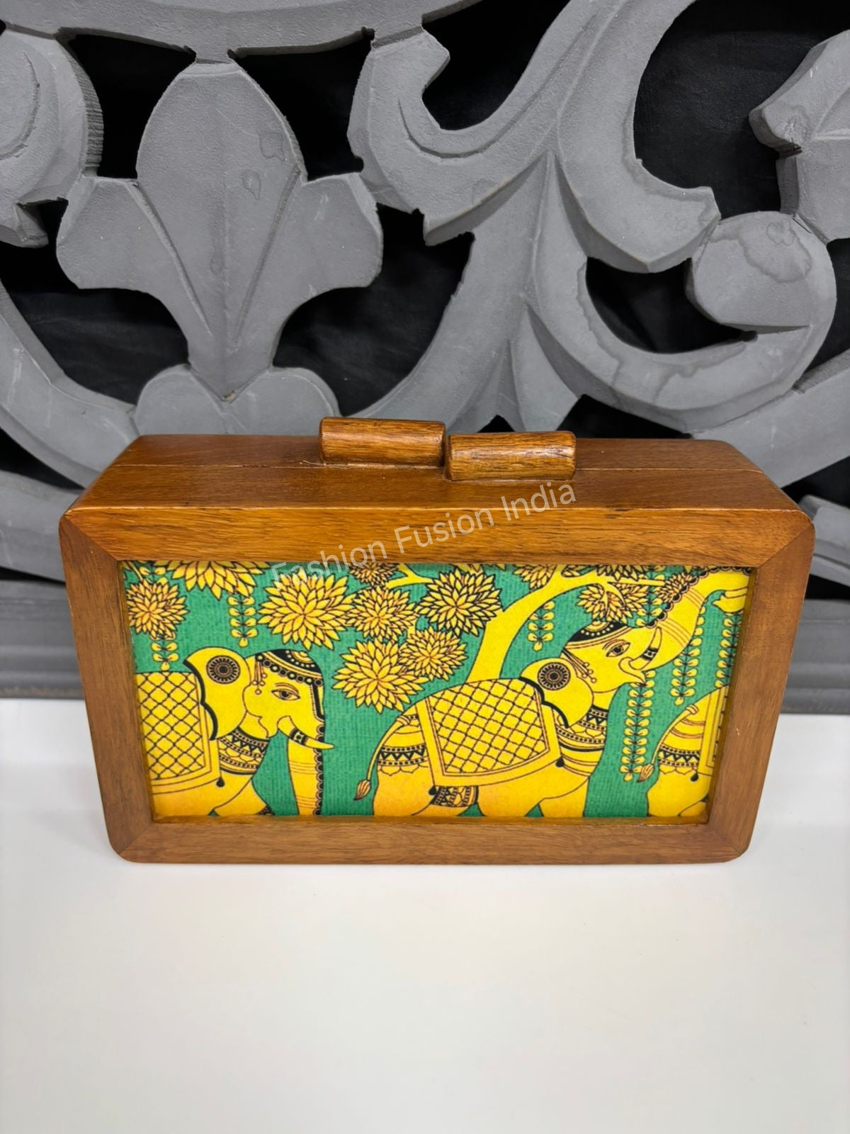 Handcrafted wooden clutch bag with ethnic elephant print on warm beige background.