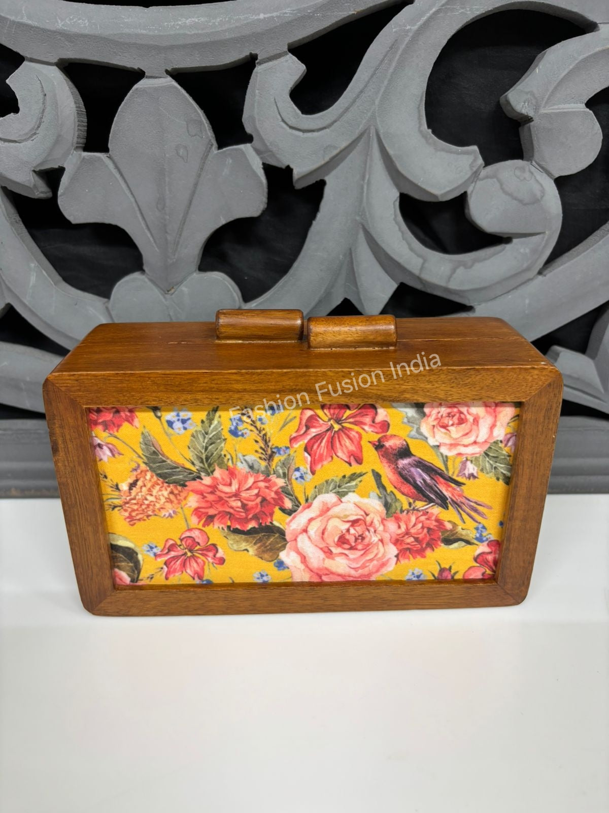 Vintage floral wooden clutch bag with bird artwork against carved grey backdrop.