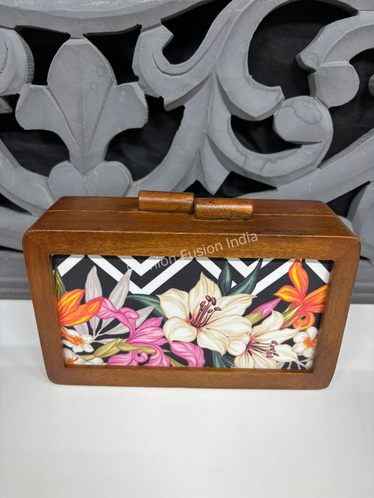 Wooden floral clutch-style box with a bold lily print, styled on a textured surface with soft décor accents.