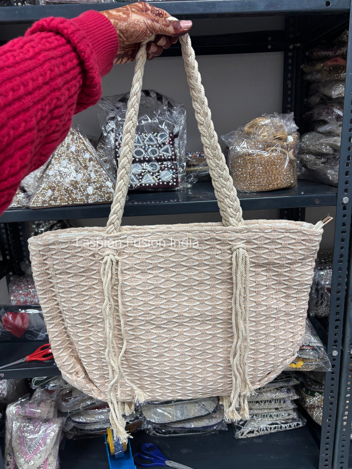 Beige woven handbag with rope handles held by a person wearing a red sweater.