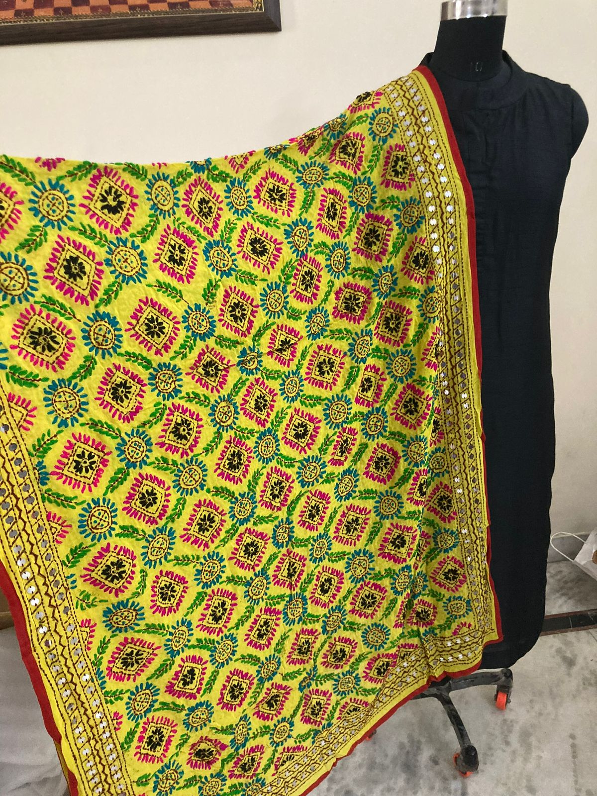 Colorful patterned fabric draped over a black garment on a mannequin against a white wall.