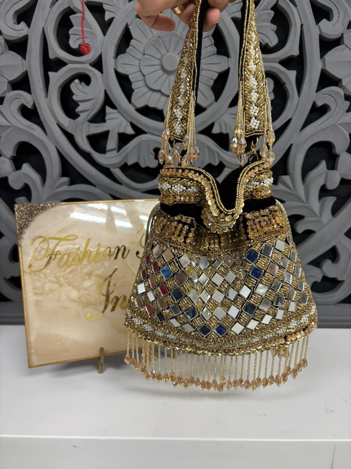Decorative handbag with intricate design and mirror work, held against a decorative wall.