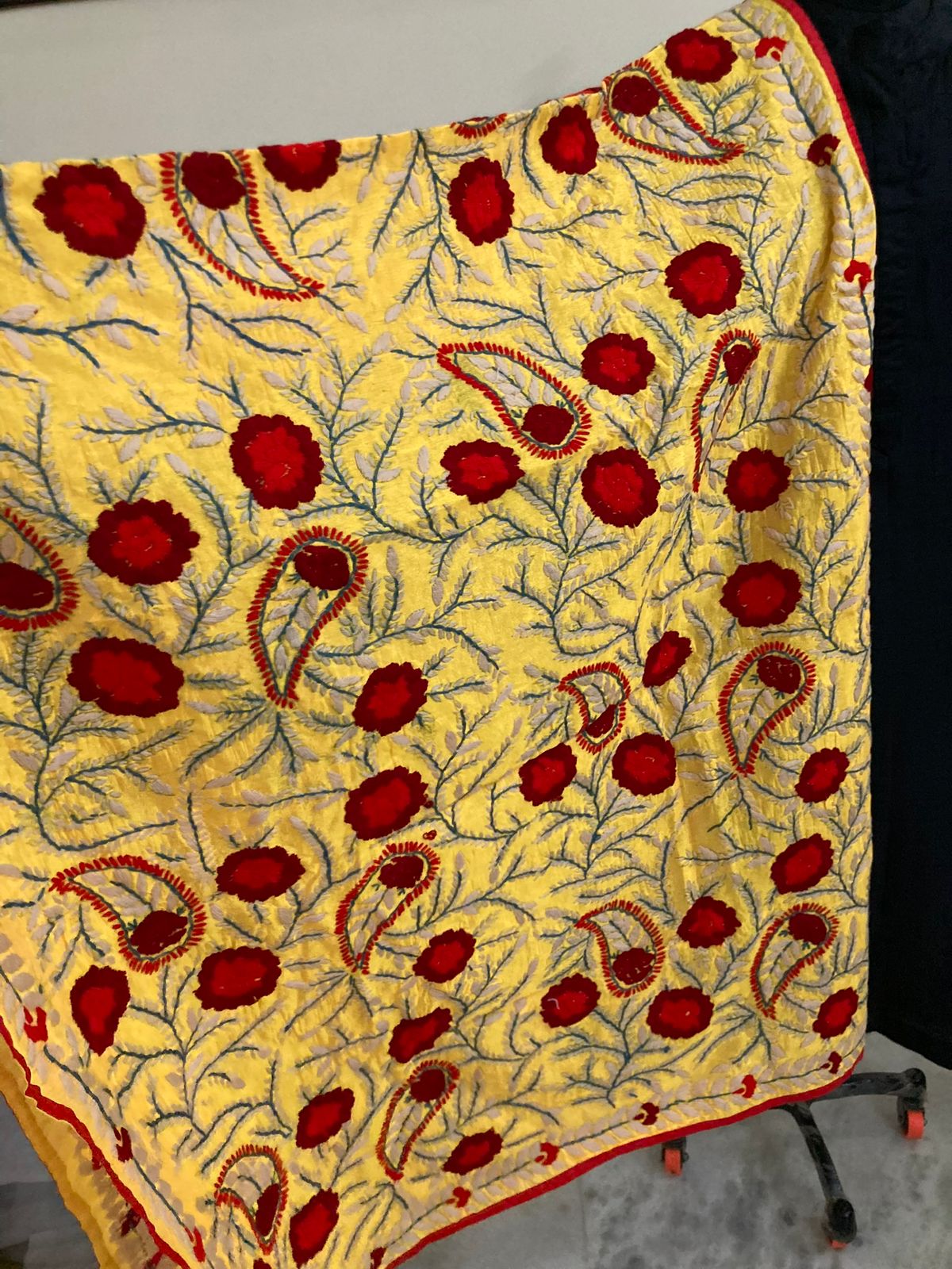 Yellow fabric with red floral embroidery on a stand against a black background