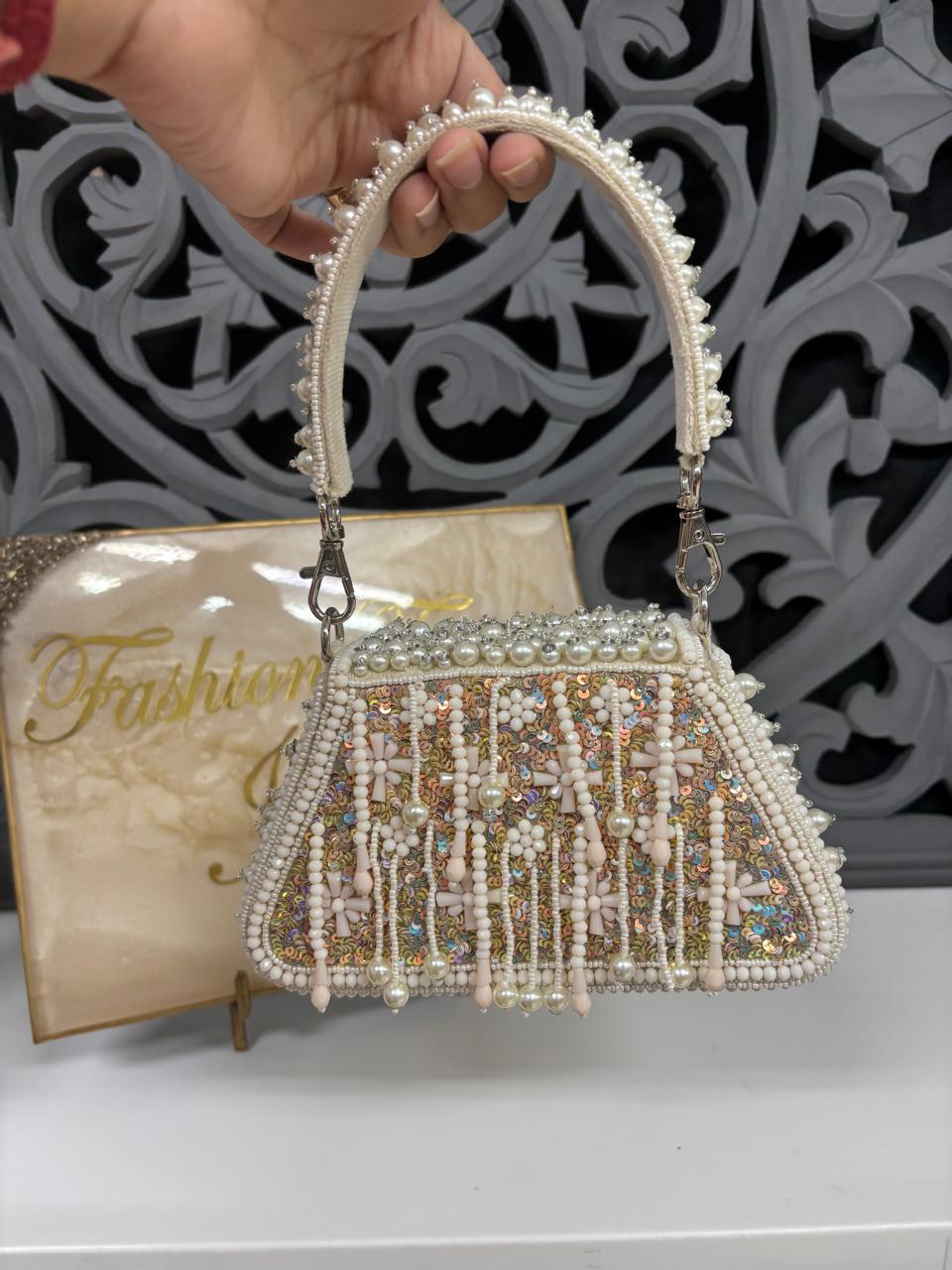 Handbag with pearl and crystal embellishments held by a hand, with a decorative background.