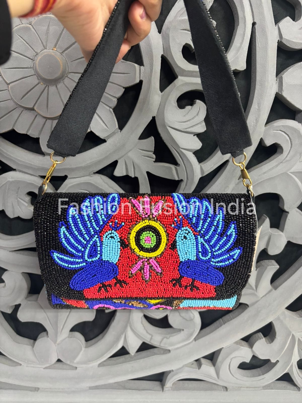 Embroidered handbag with colorful design held by a person against an ornate white and gray background.