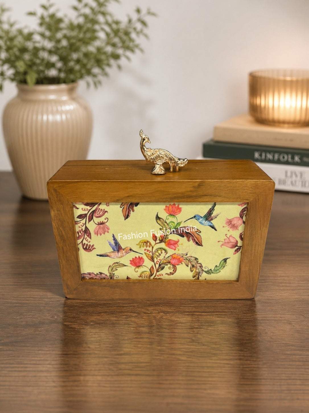 Wooden decorative box with floral bird artwork and a gold peacock handle, placed on a table with a cozy home décor background.