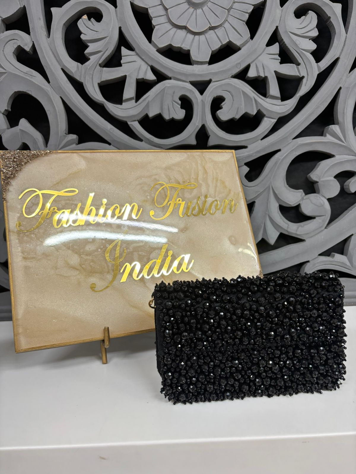 Black beaded clutch with 'Fashion Fusion India' sign in the background
