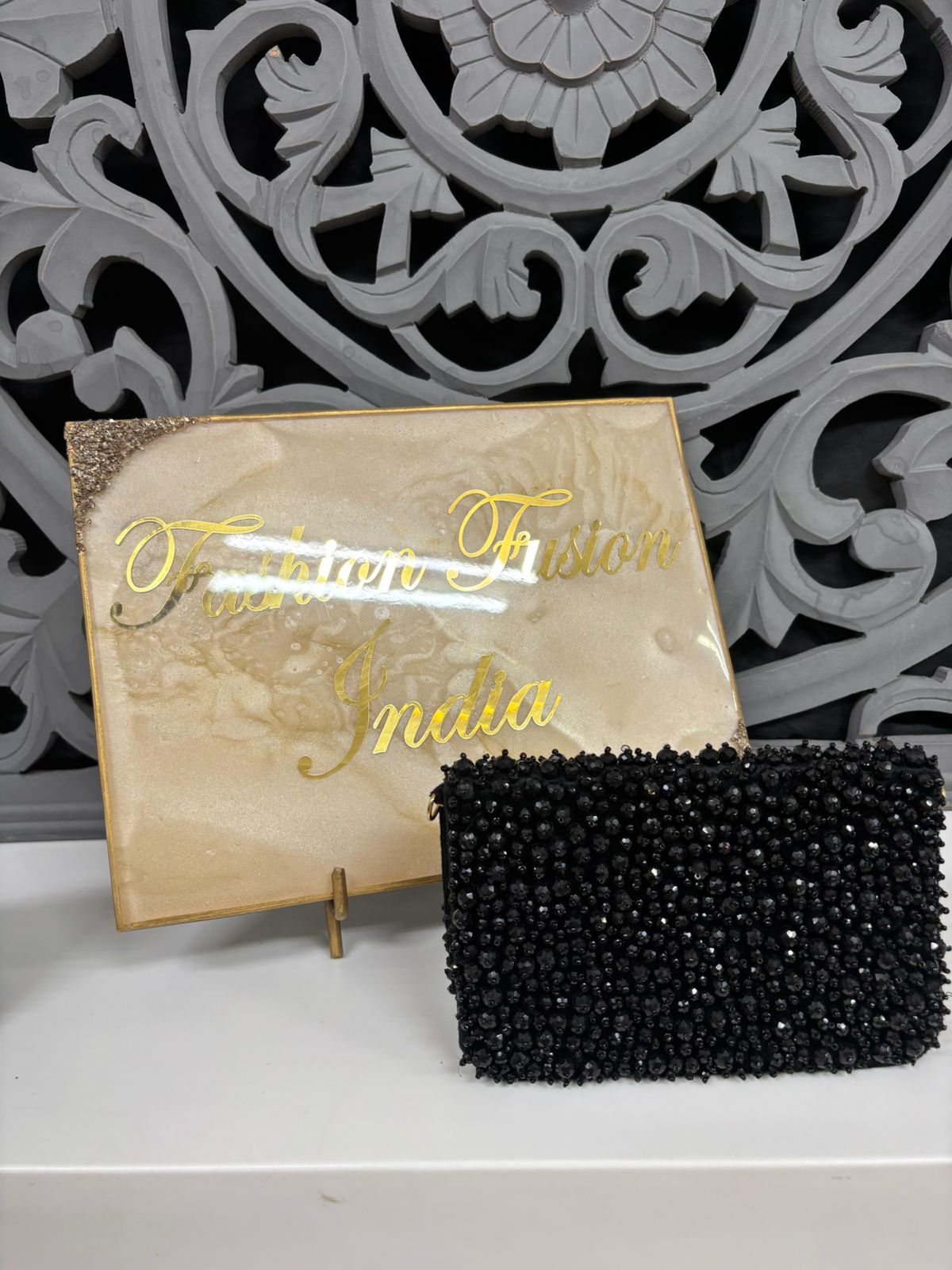 Black beaded clutch bag in front of a decorative wall with 'Fusion Fusion India' sign.