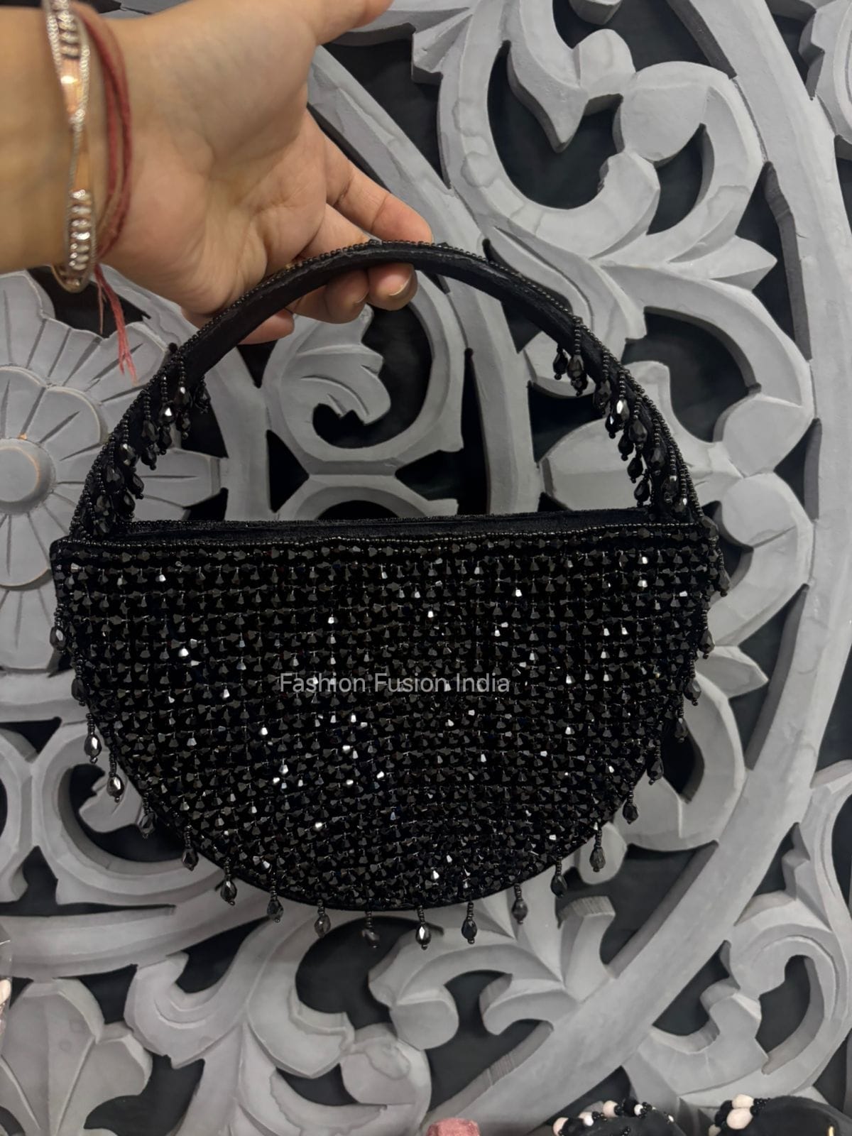 Black beaded handbag held by a hand against an ornate black and white background.