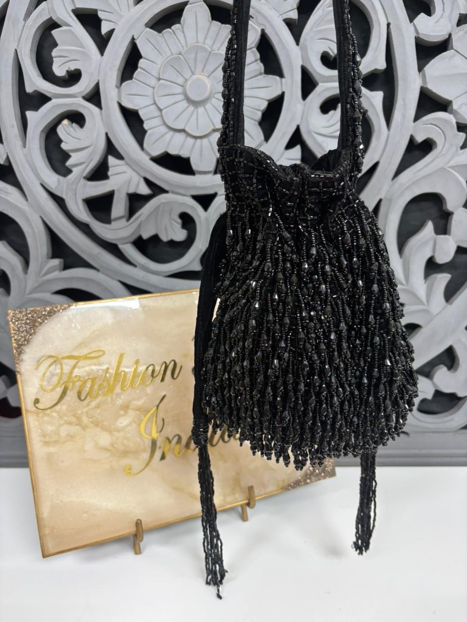 Black beaded handbag with decorative stand and 'Fashion is...' sign in the background