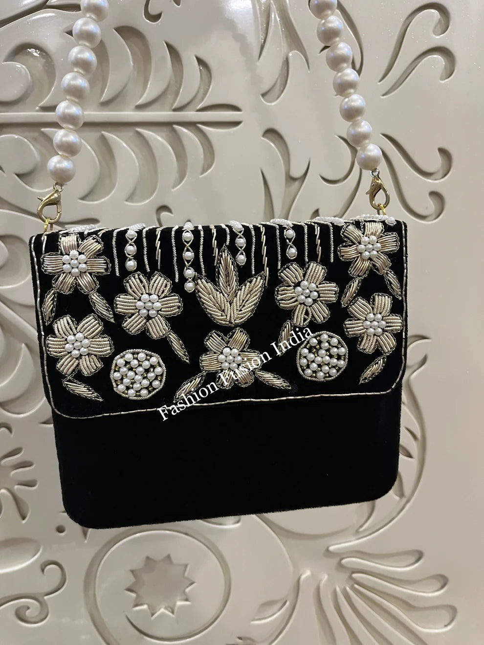 Black handbag with floral embroidery and pearl details on a decorative white background