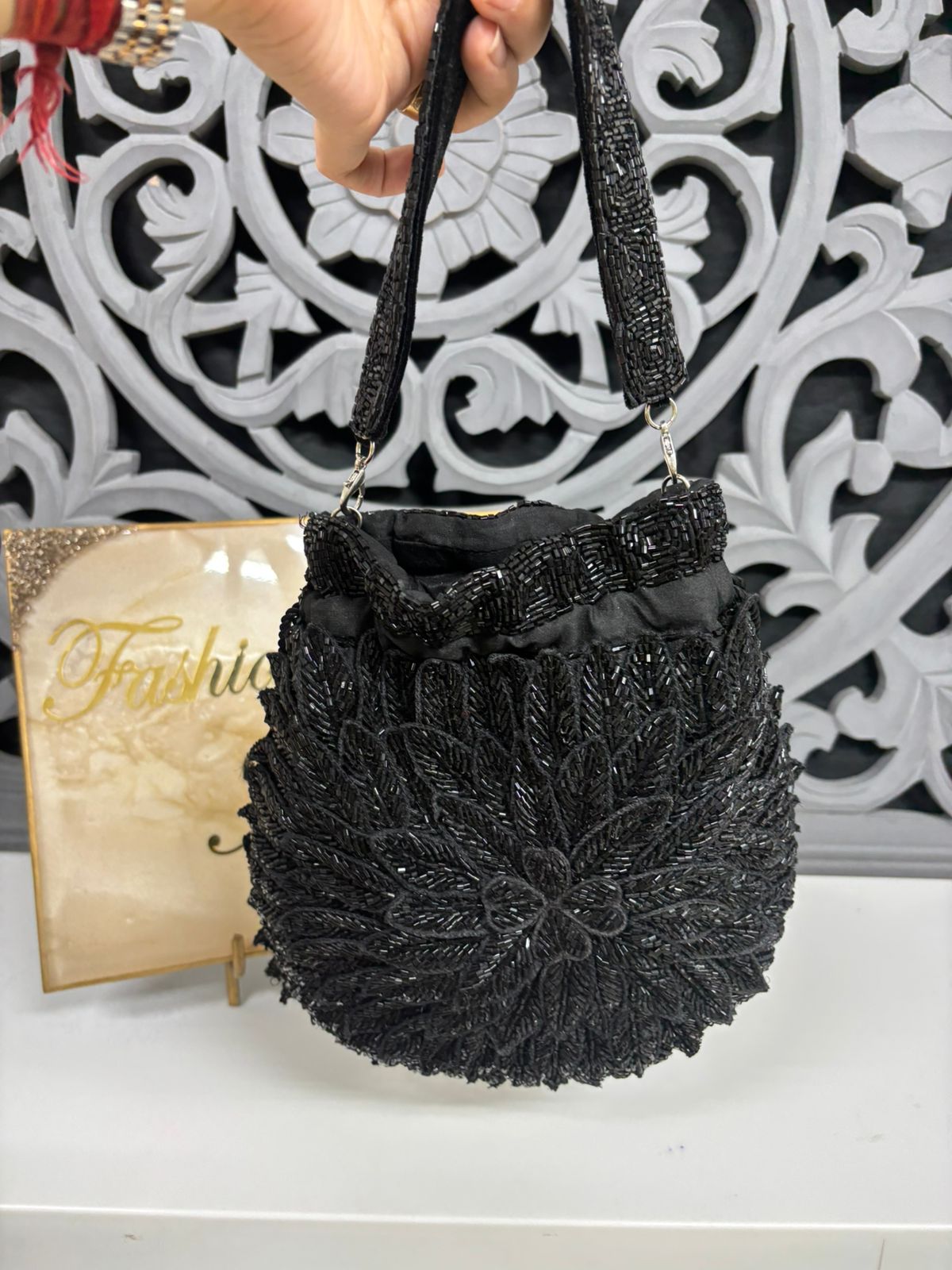 Black woven handbag held by a hand with a decorative background