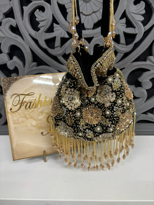 Decorative handbag with gold fringes and embellishments next to a 'Fashion' magazine on a white surface.