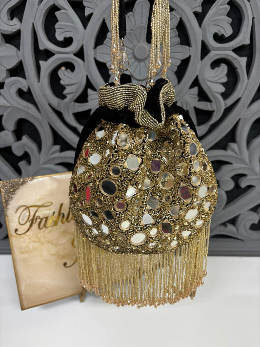Decorative handbag with gold embellishments and tassels on a white surface with a decorative gray background.