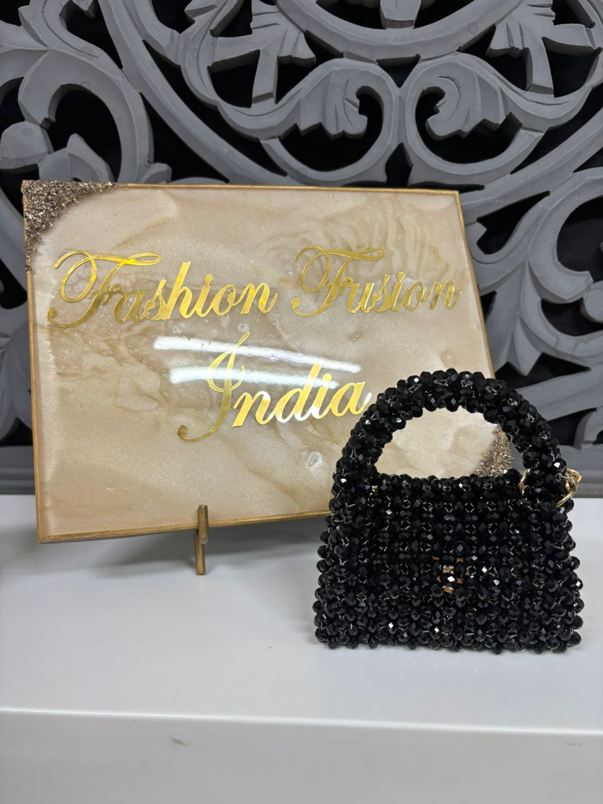 Black beaded handbag in front of a 'Fashion India' branded box.