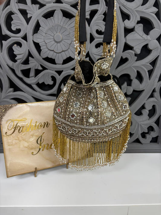 Decorative handbag with gold fringe and embellishments on a white surface with a decorative wall in the background.