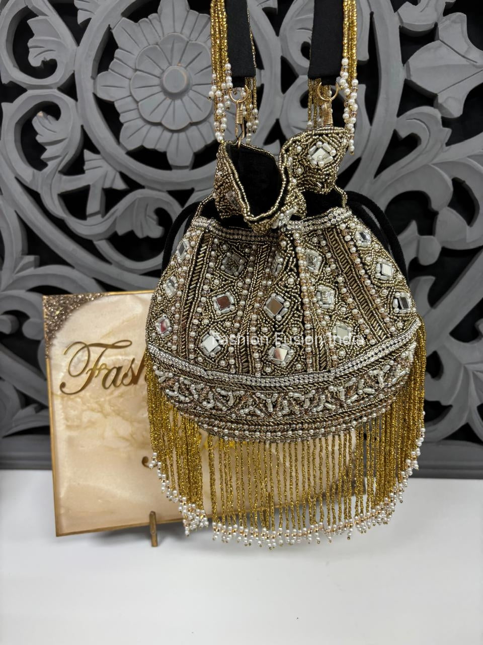Decorative handbag with gold fringe and embellishments against a decorative wall.