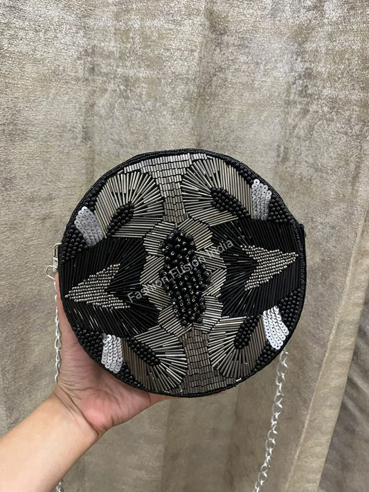 Black beaded handbag held by a hand against a textured beige background