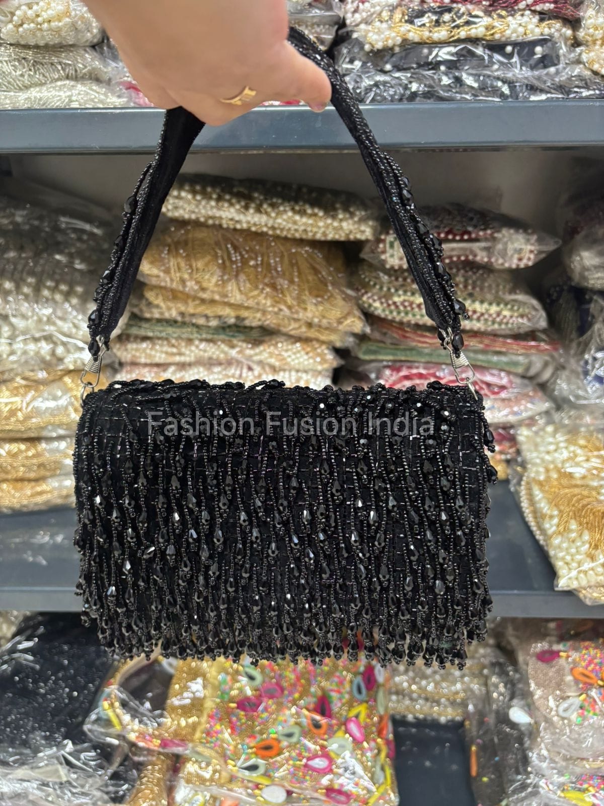 Black beaded clutch held in front of a display of embroidered fabrics.