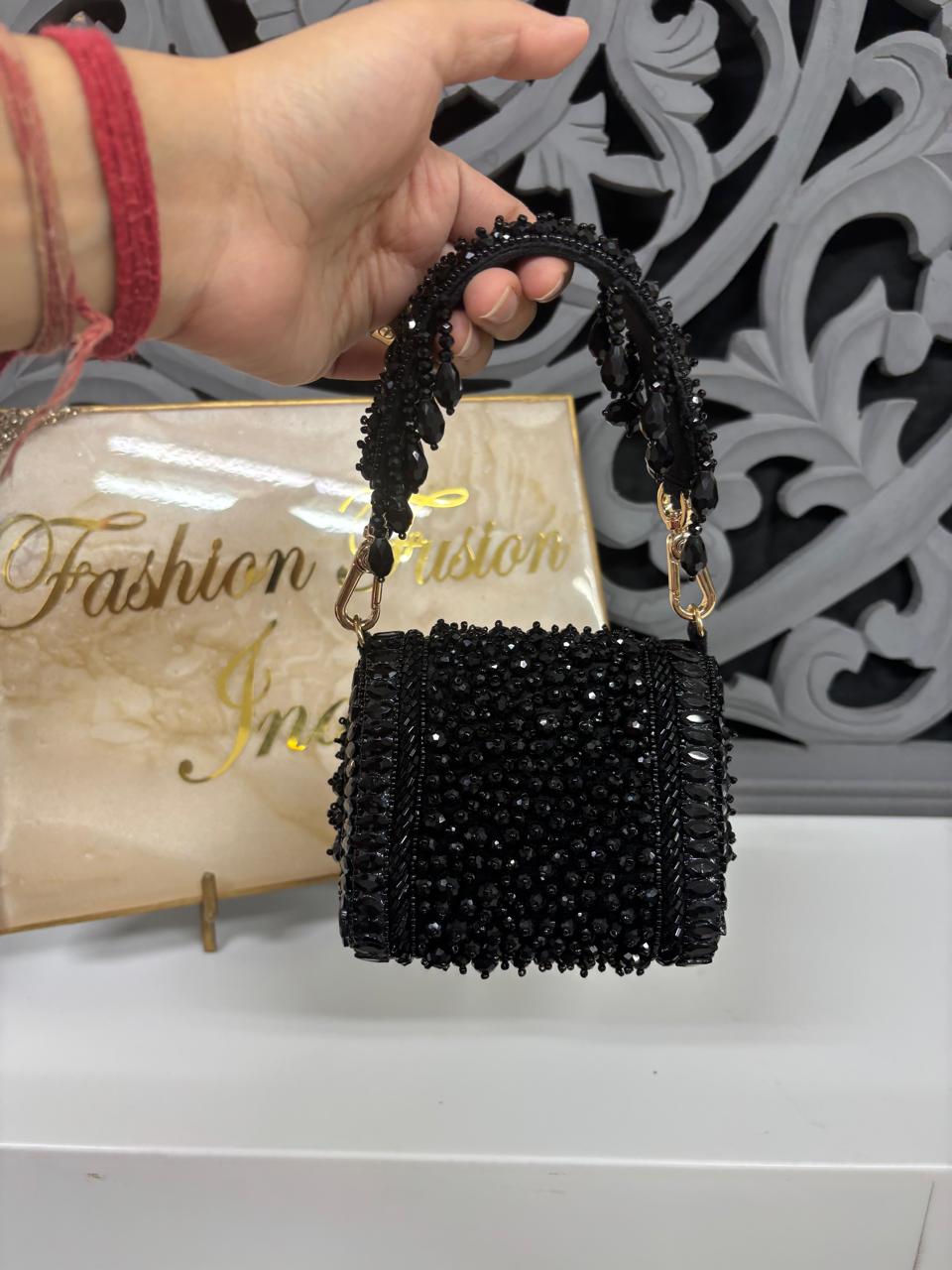 Black beaded handbag held by a hand with a red sleeve, on a white surface with 'Fashion Passion' sign.