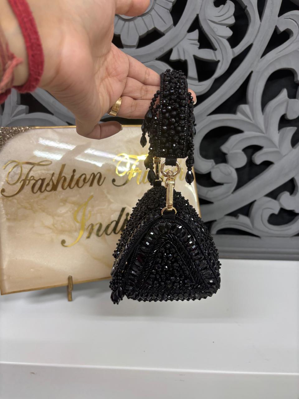 Black beaded purse held by a hand with a decorative background