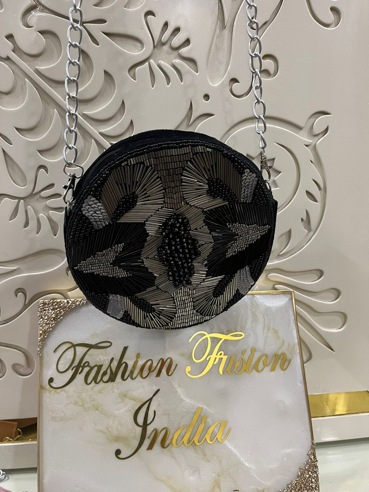 Black embroidered handbag on a stand with 'Fashion Fusion India' branding