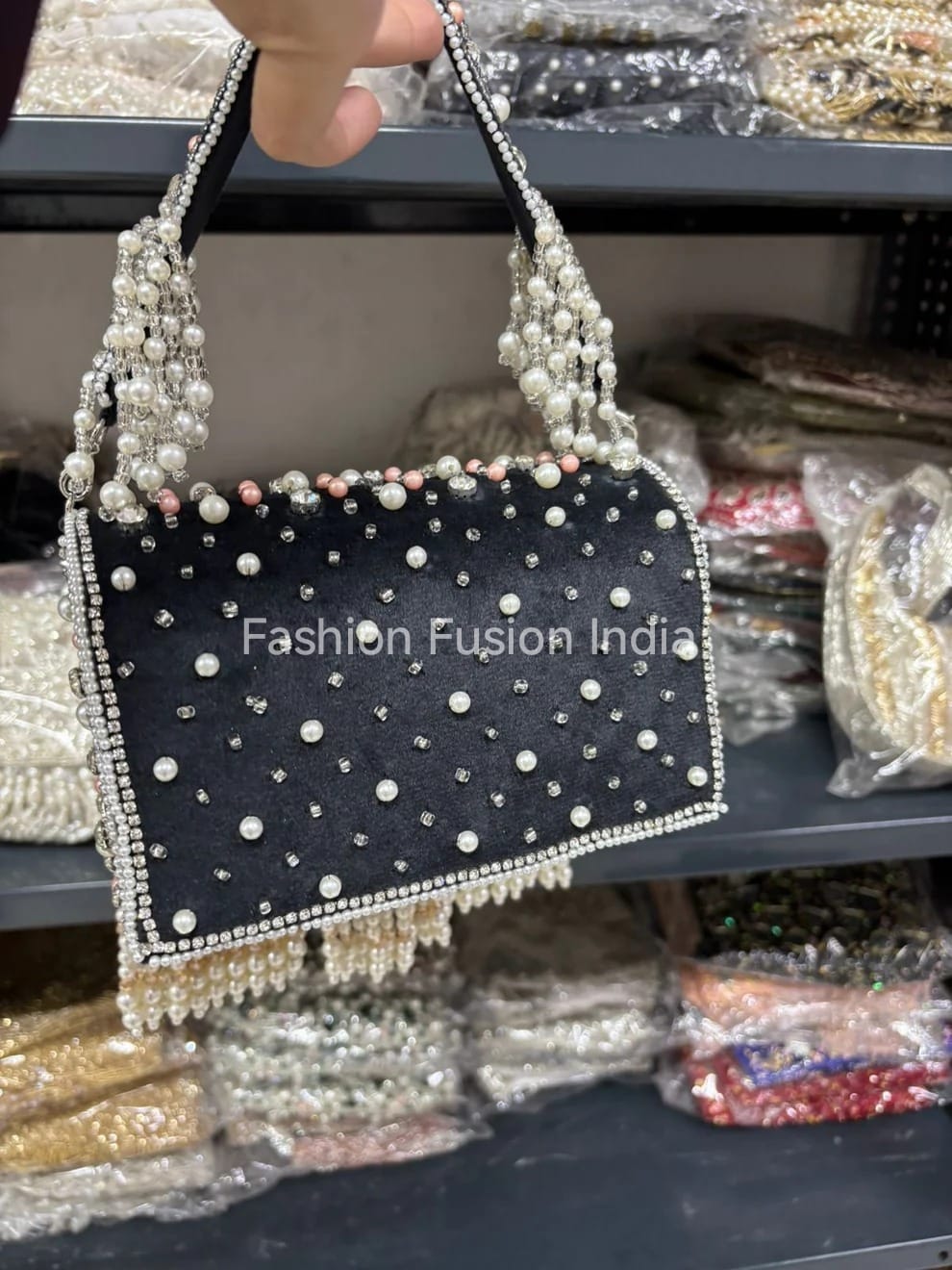 Black handbag with pearl embellishments held by a hand, with 'Fashion Fusion India' branding.