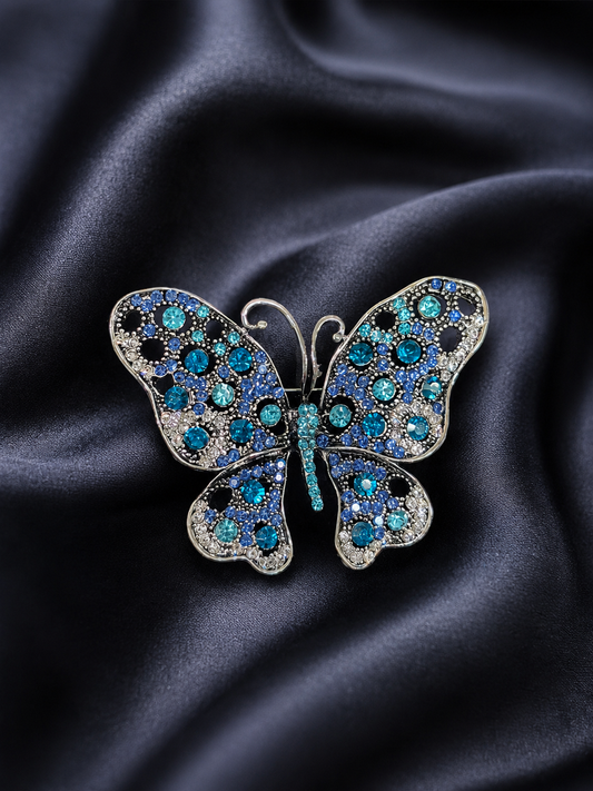 Butterfly-shaped brooch with blue gemstones on a dark fabric background