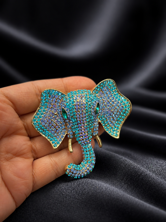 Decorative elephant brooch with turquoise stones held against a dark fabric background