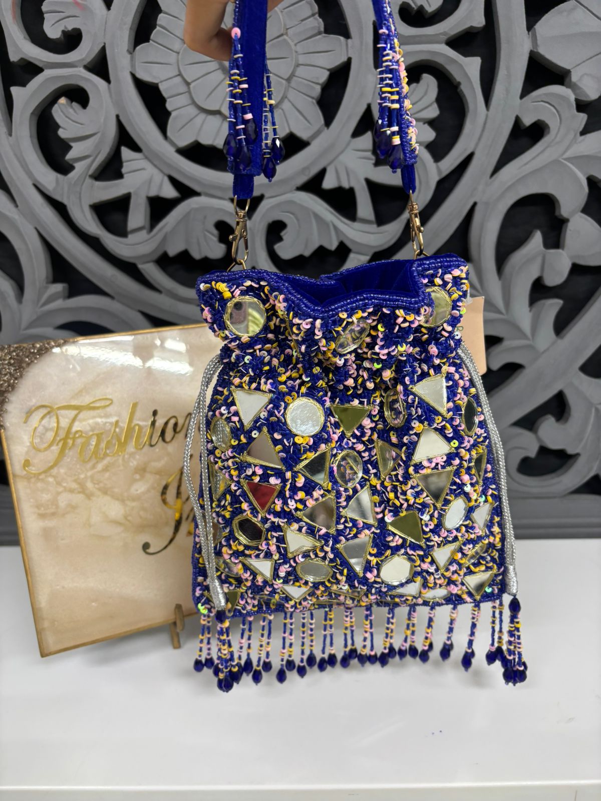Decorative handbag with blue and gold patterns on a white surface with a decorative wall in the background.