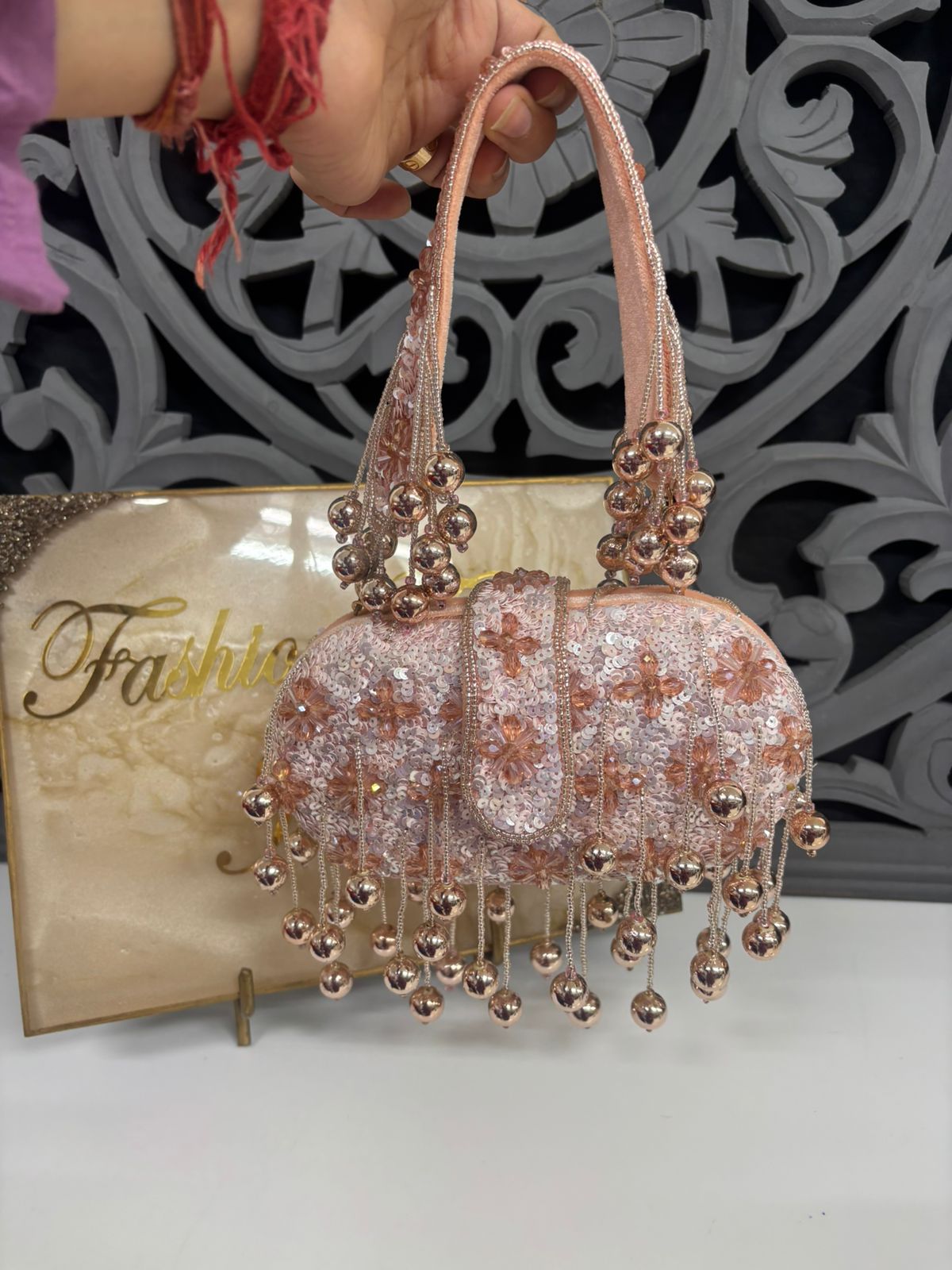 Decorative handbag with floral patterns and beaded details held by a hand, against a decorative background.