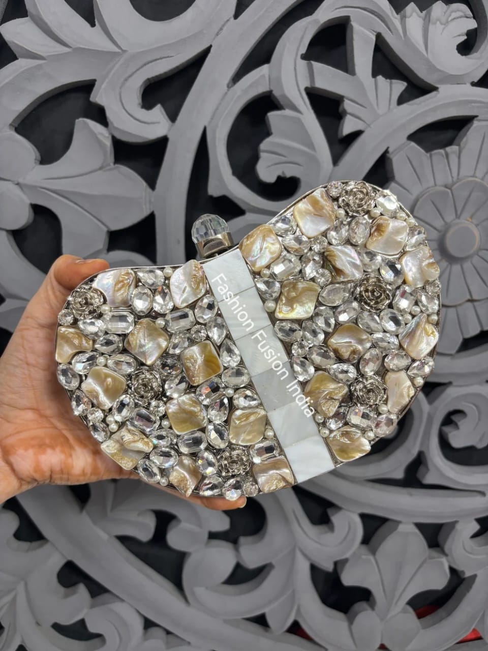 Elegant clutch bag with crystal embellishments held by a hand against a decorative gray background