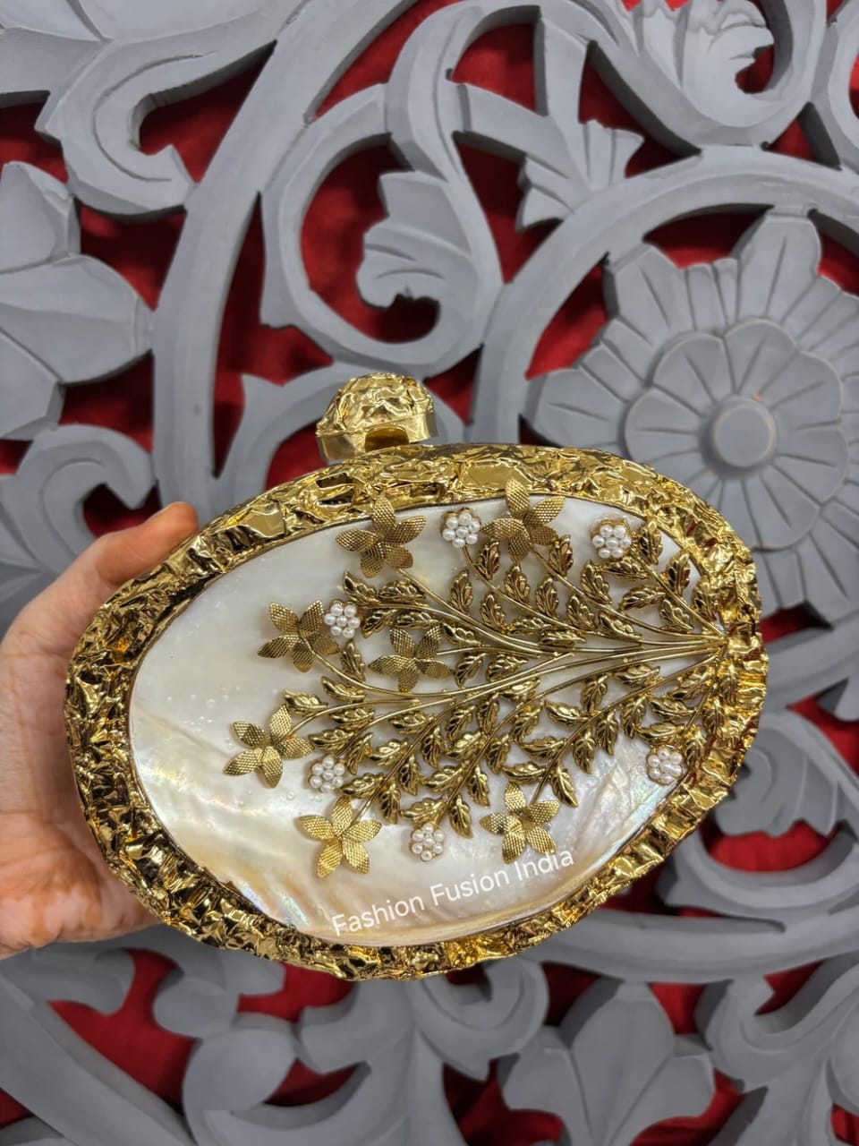 Decorative clutch with floral design held against a decorative red and white background