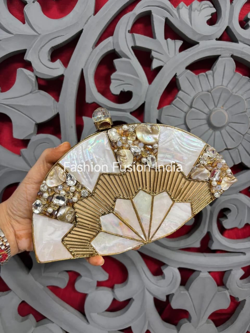 Decorative clutch with fan design and embellishments held against a decorative red and gray background.