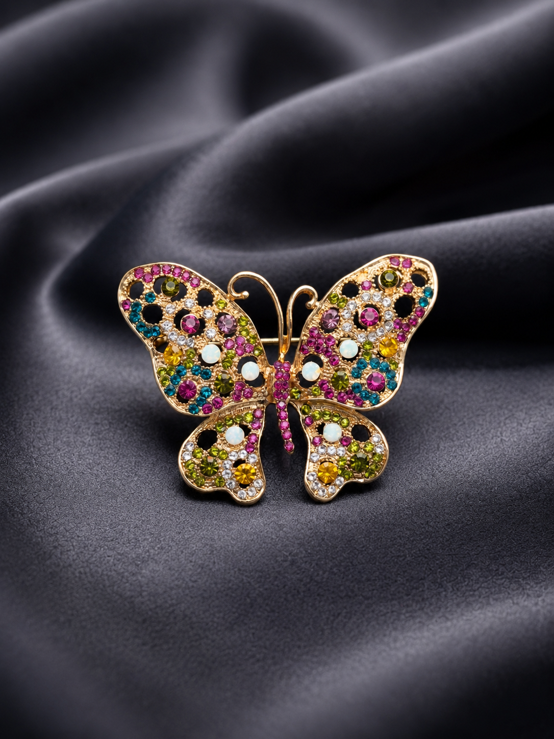 Butterfly-shaped jewelry with colorful gemstones on a dark fabric background