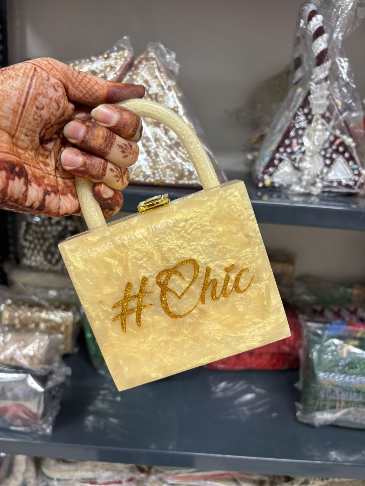 Gold handbag with '#Chic' text held by a hand against a blurred background