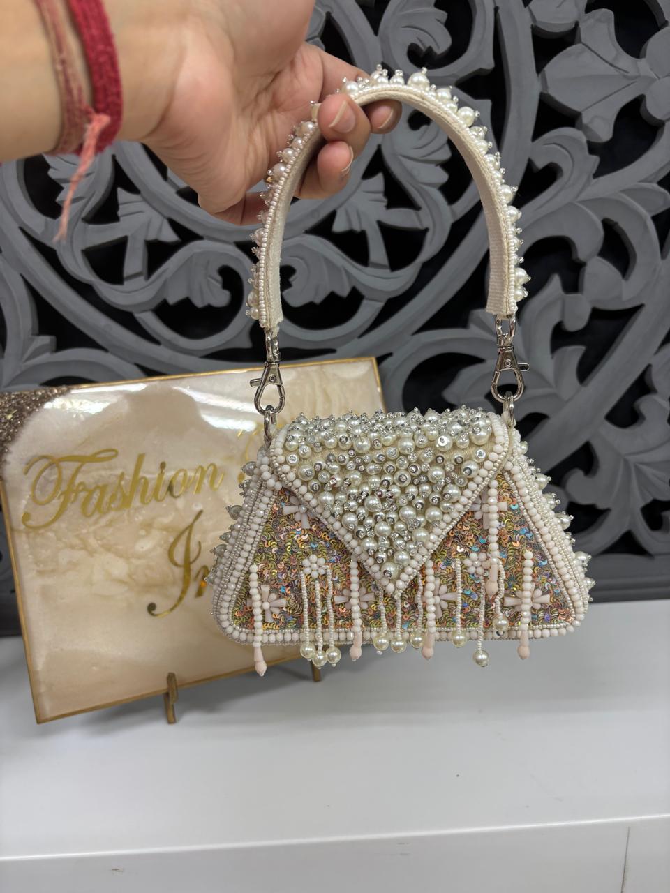 Decorative handbag with beaded details held by a hand, against a decorative wall.