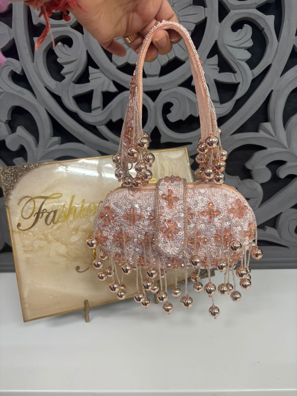Decorative handbag with beaded details on a stand with 'Fashion' magazine in the background.