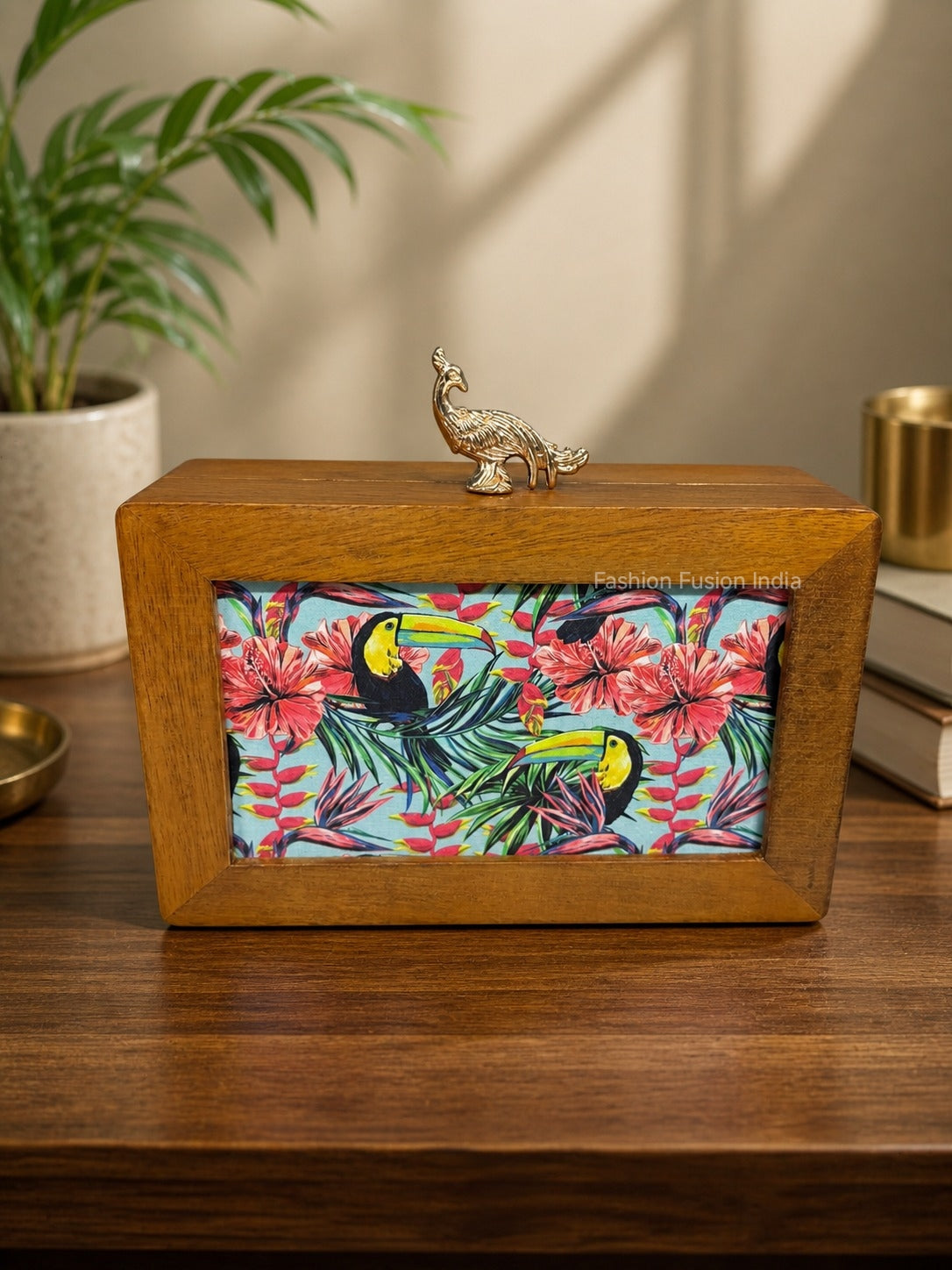 Wooden decorative box with a colorful toucan and floral print, finished with a gold peacock handle against a carved grey backdrop.