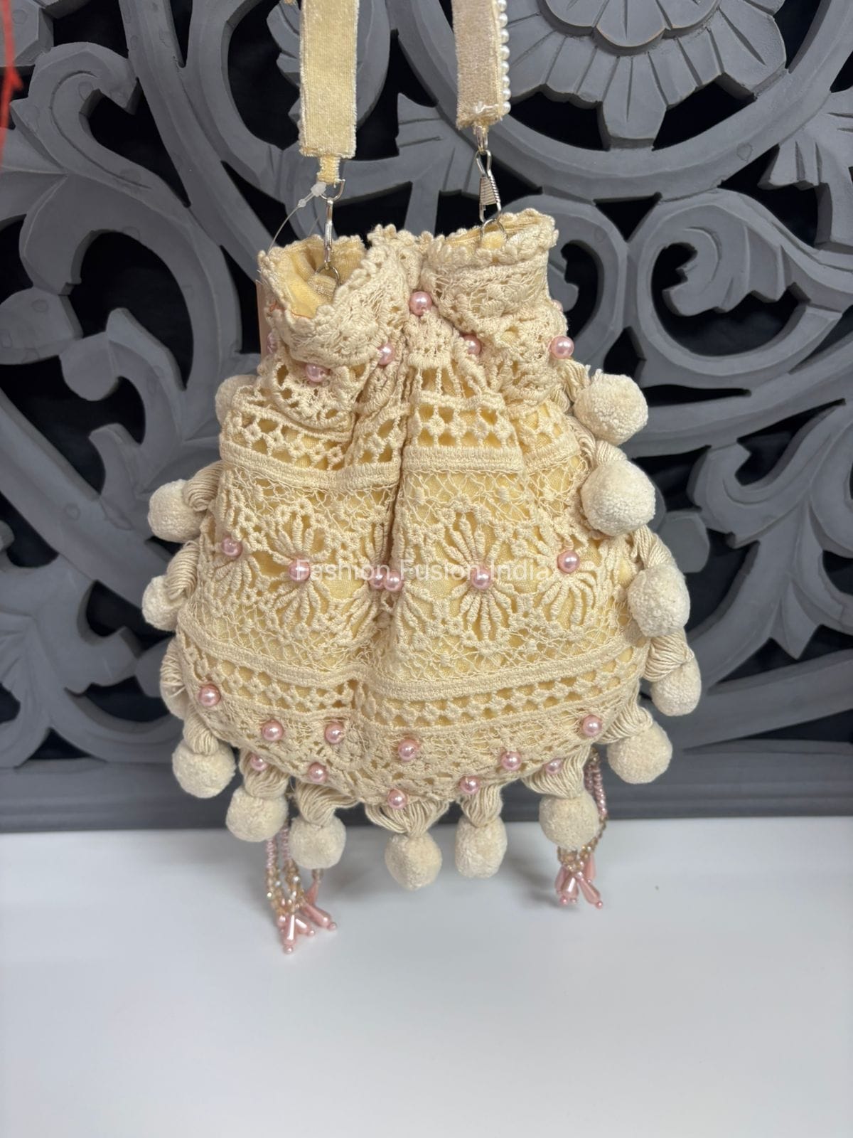 Decorative handbag with pom-poms and pink embellishments against a decorative gray background