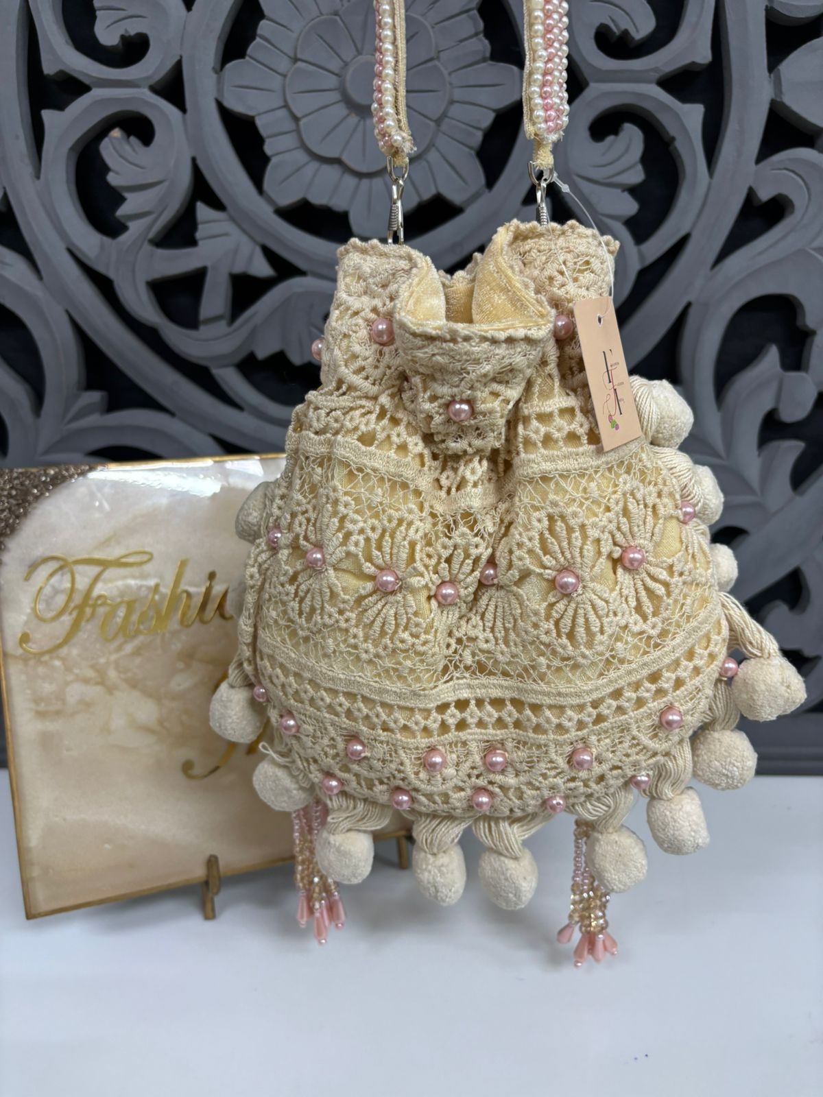 Decorative beige bag with pink beads and tassels against a decorative gray background