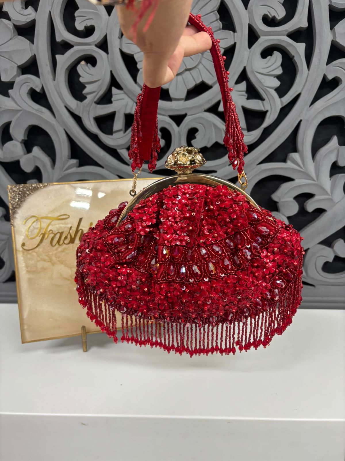Red beaded handbag with gold accents held by a person, with a 'Frash' brand card in the background.