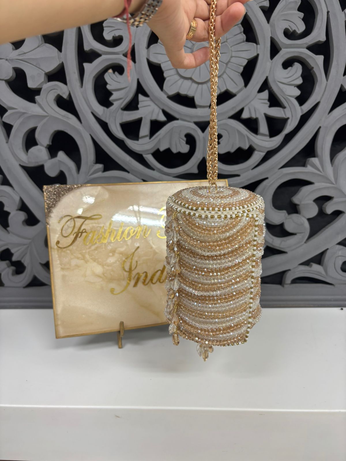 Gold beaded handbag held by a hand with a decorative background and 'Fashion India' sign.