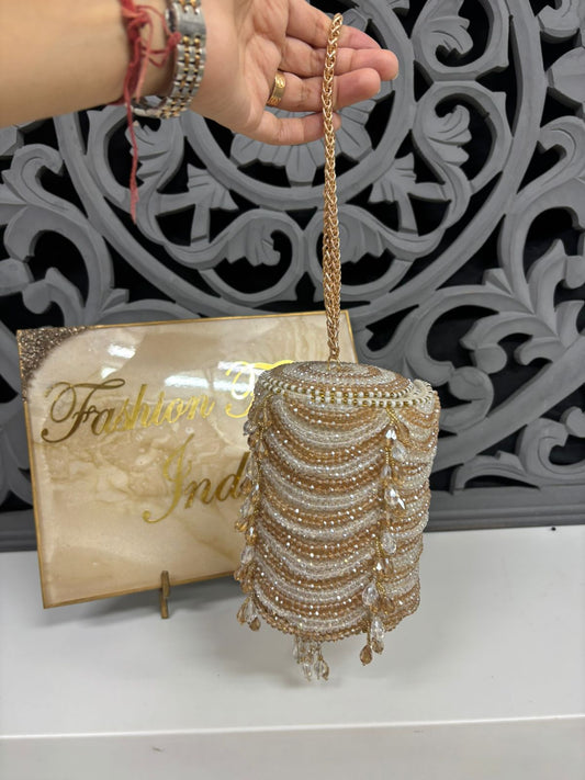 Handbag with decorative chain and beads held by a hand, with 'Fashion India' sign in the background.